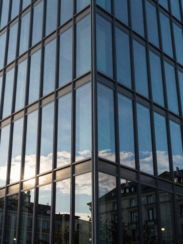 Photographie en gros plan de l'angle d'un bâtiment moderne en verre à Genève, reflets nets du ciel bleu, ombres géométriques précises, style suisse.