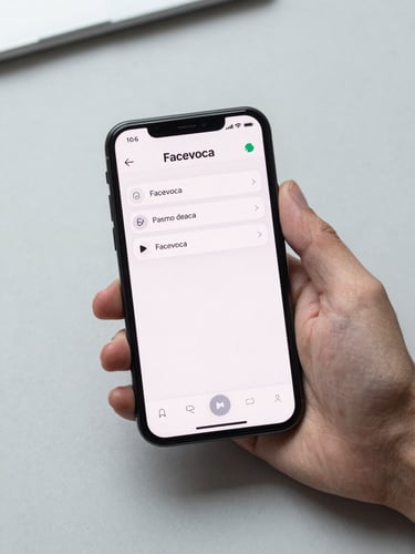 Direct overhead view of a modern Android smartphone held in a right hand against a clean light-gray desk surface, the Facevoca app interface visible on screen — voice memo list with clean typography, diffuse studio lighting, no shadows