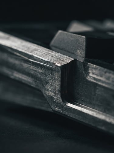 Extreme close-up macro shot of a precision-milled aluminum keyboard side profile, raw metallic texture, low-key directional side-lighting, deep charcoal shadows, sharp focus