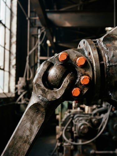 Close-up of a heavy industrial mechanical joint with safety orange bolts, dramatic factory window light, high-contrast metallic tones, sharp focus, 35mm lens