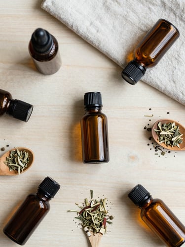 Overhead flat-lay of amber glass tincture bottles, loose dried herbs, wooden spoon, and linen fabric on a clean oak table, soft diffused daylight, muted sage and cream tones.