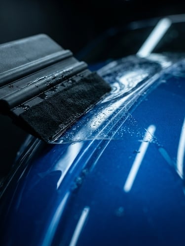 Extreme close-up of a squeegee smoothing high-gloss paint protection film over a clean sports car fender, crisp studio lighting, electric blue highlights, water droplets.
