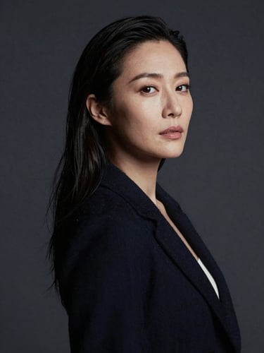 Moody low-contrast professional portrait of a female art director in a dark studio, dramatic side lighting casting soft shadows, editorial style, charcoal background.