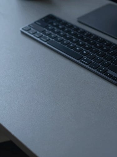 A clean, empty, organized workspace with a modern keyboard on a slate-gray desk, cool diffused daylight, low contrast, desaturated navy tones.