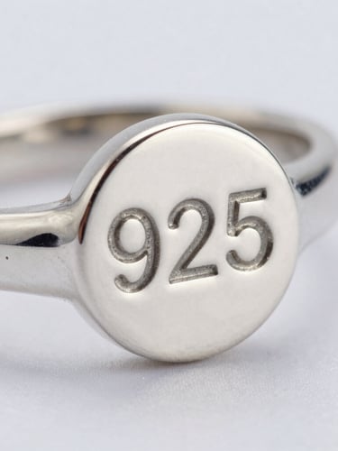 Extreme close-up of a 925 hallmark stamp on a minimalist silver ring, cool diffused daylight, sharp metallic highlights, macro lens.