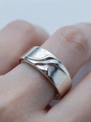 Extreme macro close-up of a sculpted 925 sterling silver ring on a finger, cool diffused daylight, crisp metallic highlights, shallow depth of field