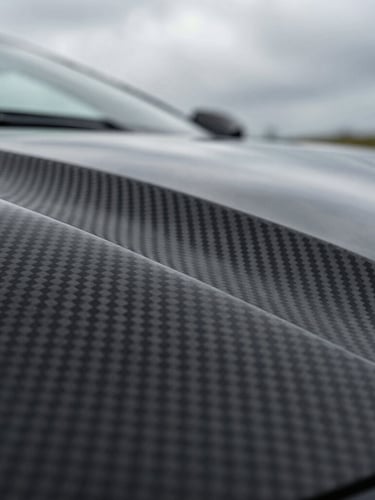 Extreme close-up of a hypercar's carbon fiber weave panel under dramatic overcast daylight, sharp lines, ultra-premium texture.