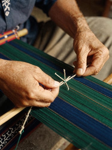Close-up of artisan hands weaving traditional ikat under soft golden hour light, rich threads of indigo and forest green, 35mm film.
