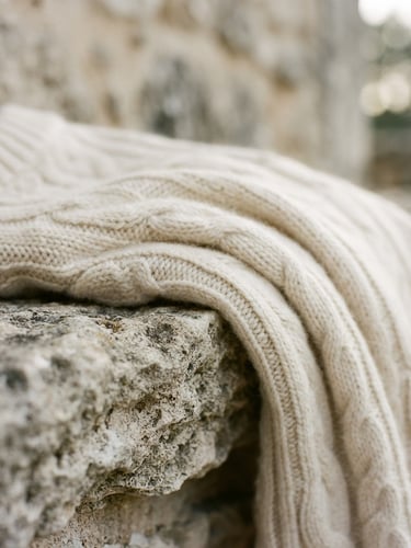 Macro close-up of a heavy cream cashmere knit garment draped over a limestone ledge, soft morning daylight, shallow depth of field, 35mm film style