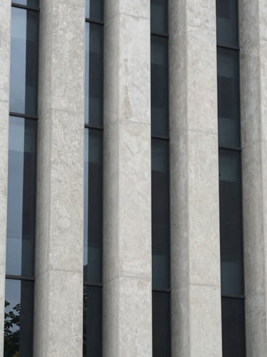 Symmetrical architectural crop of towering concrete columns and glass panels under overcast light, clean structural lines