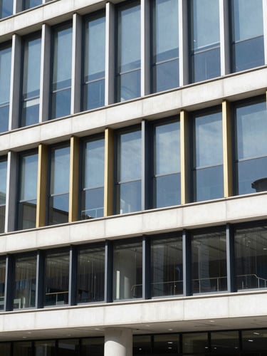Architectural shot of a modern institutional building facade with clean glass lines, bright natural daylight, deep navy shadows, 35mm editorial photography
