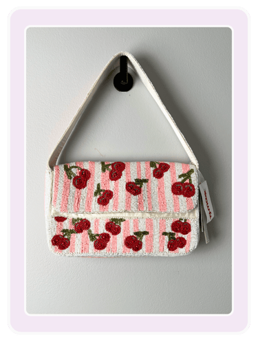 A white and pink striped beaded shoulder bag with a red cherry pattern hanging on a hook.