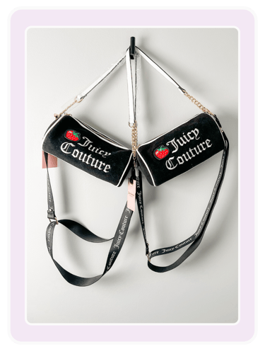 Two black Juicy Couture barrel crossbody bags with strawberry patches hanging on a wall.