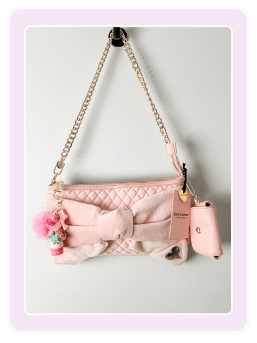 Light pink Juicy Couture quilted shoulder bag with velvet bow and gold chain strap hanging on a wall.