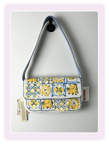 Handcrafted beaded shoulder bag with yellow floral designs and a blue gingham strap hanging on a wall.
