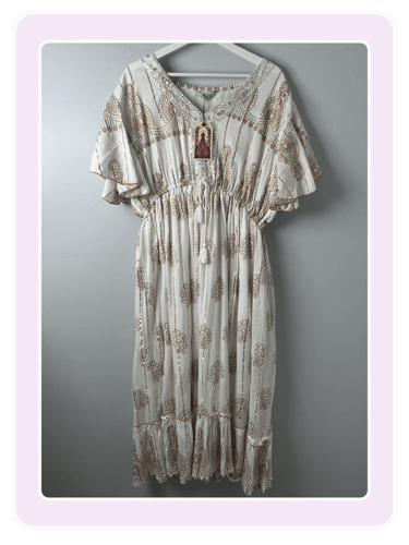 White boho maxi dress with gold floral print and lace V-neck hanging on a hanger.