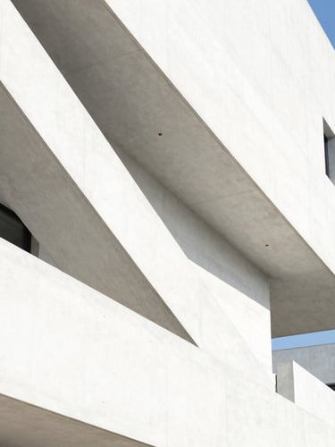 Bright architectural photography of a stark white modern concrete building with sharp diagonal shadows under intense direct sunlight, 35mm