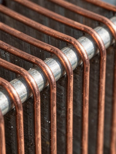 Macro close-up of copper refrigerator condenser coils, bright direct daylight, sharp focus on metallic textures and technical details.