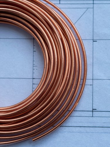 Top-down macro photography of clean copper wire scrap and blueprint lines, high-contrast cool daylight with metallic copper highlights, sharp focus, 35mm lens