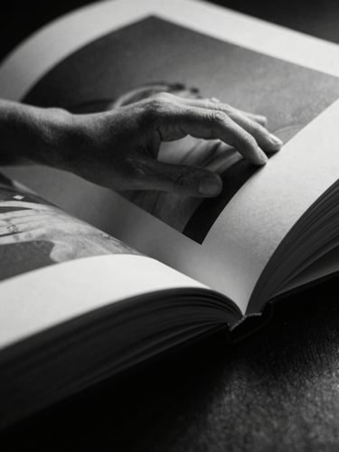 Mãos delicadamente folheando as páginas de um livro de arte em preto e branco, close-up abstrato de uma imagem de corpo em alto contraste, luz dramática.
