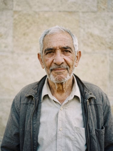 Dignified candid portrait of an elder community leader in soft natural daylight, warm stone background, medium format film style
