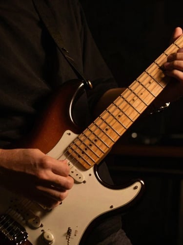 Close-up of hands navigating the fretboard of an electric guitar, low-key dramatic studio lighting, warm amber backlights, deep shadows