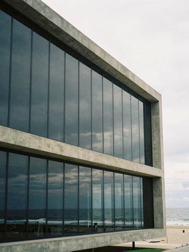 Wide architectural shot of a modern minimalist concrete and glass facade in Balneário Camboriú, soft overcast coastal daylight, ocean reflection on glass, medium format film
