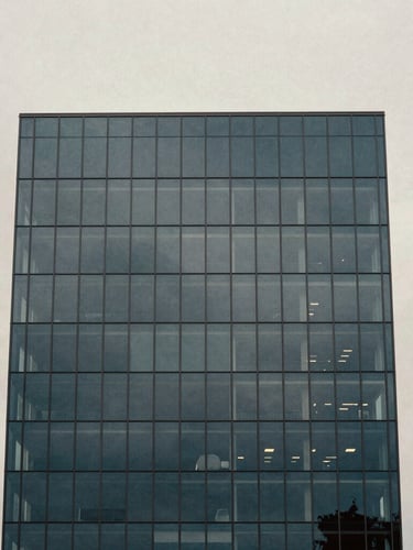 Minimalist architectural photography of a modern coastal glass tower facade reflecting soft overcast daylight, deep slate tones, medium format film