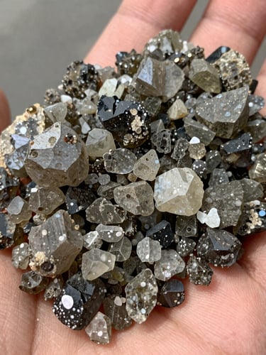 Macro shot of raw gray-olive zeolite mineral granules held in a hand, bright natural daylight, sharp focus on crystalline geological texture.