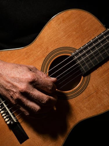 Dramatic chiaroscuro close-up of a guitarist's hand executing an alzapúa on a cypress flamenco guitar, deep shadows, warm wood tones, 35mm film grain