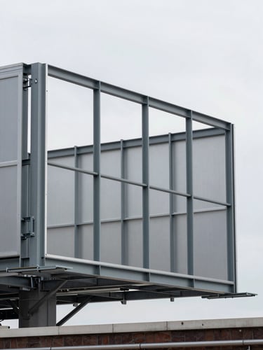 Close-up architectural shot of a large billboard frame structure mid-installation on an urban rooftop, steel mounting brackets and aluminum panel edges visible in sharp detail, overcast natural daylight from the north, no workers or people in frame, flat even lighting across the metal surfaces