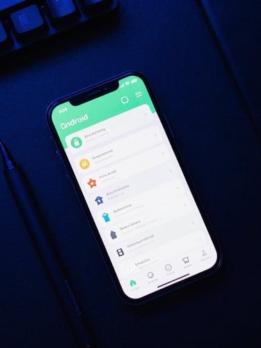 Overhead flat-lay of a developer workspace with ambient neon-blue lighting, featuring a modern Android phone displaying a clean, responsive user interface