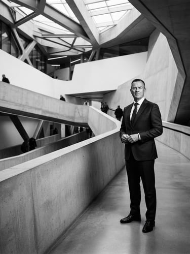High-contrast black and white executive portrait of a senior transformation leader in a modern architectural setting, cool slate tones, sharp editorial lighting, wide environmental framing