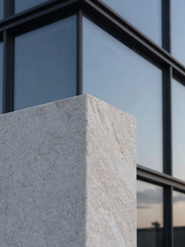Close-up architectural detail of raw travertine marble and dark structural glass reflecting a twilight sky, sharp angles, clean lines, minimalist luxury.