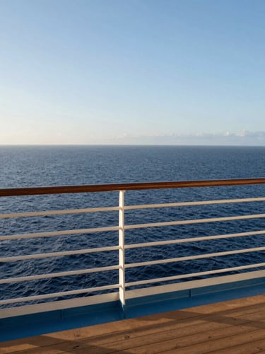 A private teak balcony on a cruise ship looking out over a calm, deep blue ocean at sunrise, clean minimalist framing.