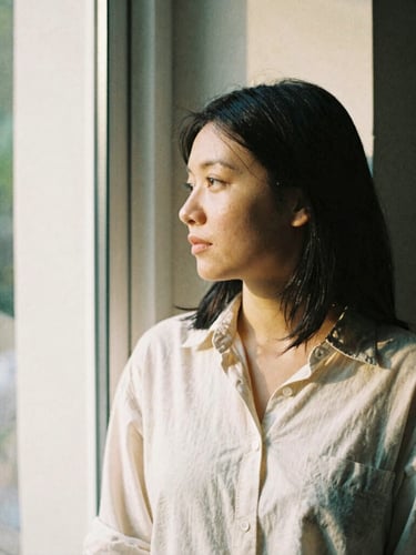 Thoughtful 35mm portrait of a creative founder looking out a window, soft directional window light, natural shadows, warm editorial tones.