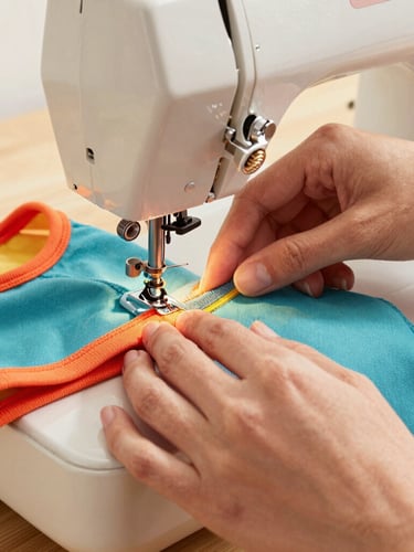 Close-up of hands sewing colorful pet clothing on a vintage sewing machine, bright warm daylight, focus on the textile textures and precise stitching