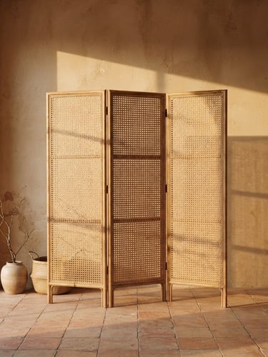 Straight-on architectural shot of a folding rattan screen casting long afternoon shadows on a soft sand wall, 35mm warm editorial photography.