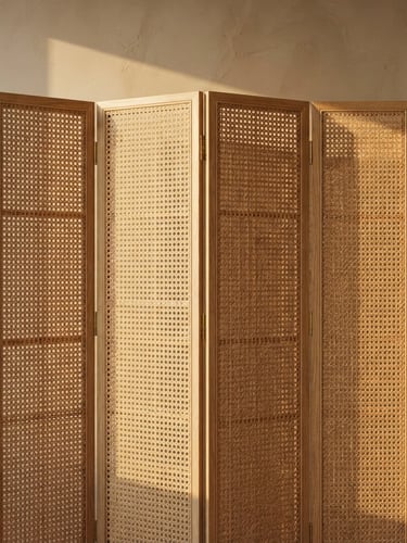 A straight-on architectural detail shot of a folding rattan screen catching warm, low-angle afternoon sunlight, casting soft long shadows on a neutral sand wall, 35mm.