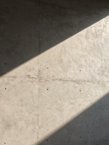 Architectural detail of a sunlit concrete wall casting sharp diagonal shadows, minimal and clean, warm afternoon light.