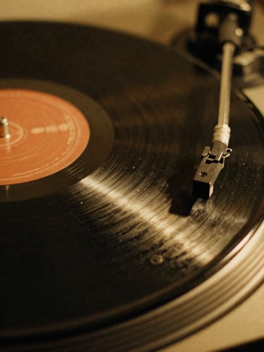 Macro close-up of vinyl record grooves spinning on a turntable, low-key side lighting with a warm golden glow, dust particles visible in the light, 35mm film grain.