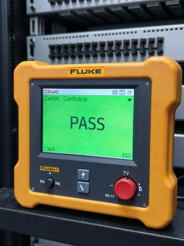 A Fluke network tester screen showing a bright green PASS result on a Cat6A certification test in a clean server room.