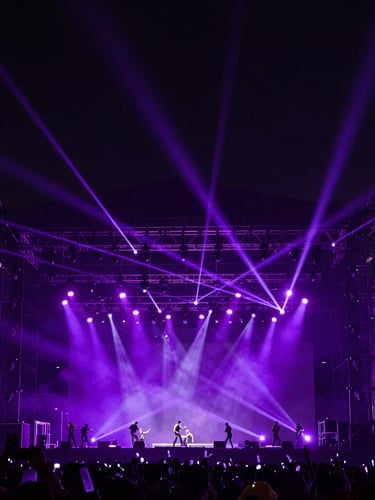 Wide-angle dramatic shot of massive festival rigging and stage lights, deep navy and electric violet tones, high-contrast laser beams cutting through haze