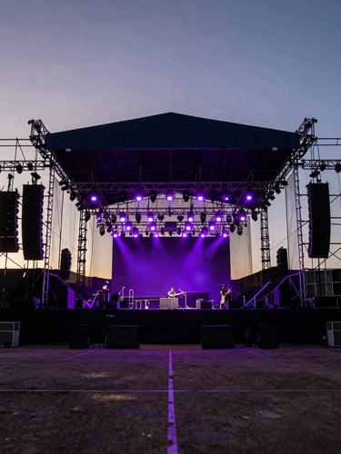 Wide-angle environmental shot of festival rigging and line arrays at sunset, empty stage waiting for soundcheck, dramatic backlighting.