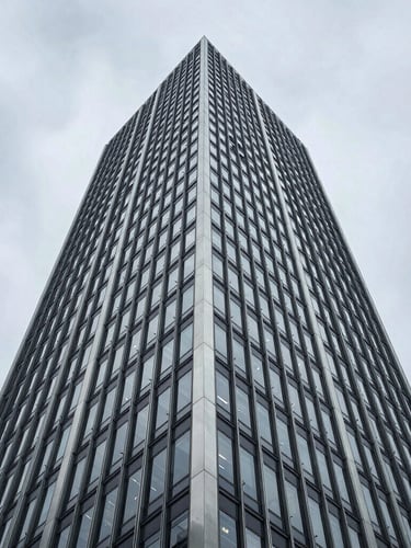 Extreme low-angle architectural shot of a brutalist steel and glass skyscraper facade rising into an overcast metropolitan sky, sharp geometric lines, cool-toned natural light.