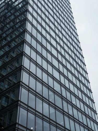 Low-angle architectural crop of a modernist steel-and-glass skyscraper facade under cool overcast light, sharp geometric shadows, minimal composition