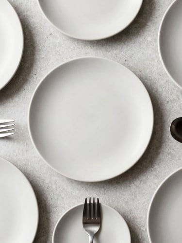 Sharp, geometric top-down flat lay of matte ceramic plates and brushed steel utensils resting on a clean light gray stone countertop, soft natural morning light, 35mm lens
