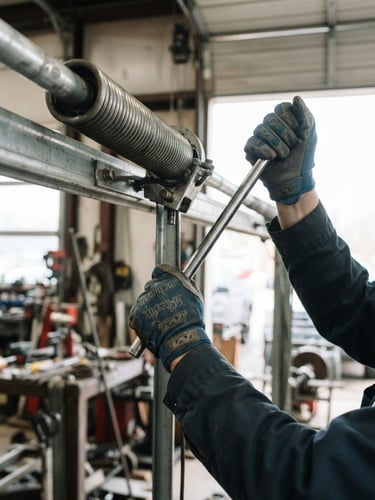 Close-up of a technician's gloved hands safely working on a garage door torsion spring, bright natural light, industrial setting, 50mm lens, sharp focus