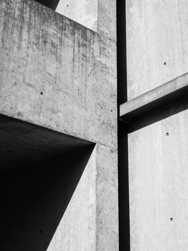 Stark brutalist photography, harsh industrial shadows, high-contrast black and white, close-up of raw textured concrete meeting unpolished steel, 35mm