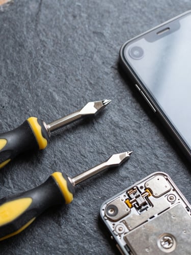 Top-down flat lay of precision screwdrivers and a disassembled smartphone on a dark slate workbench, cool bright lighting, high contrast technical details